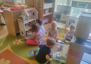 Pięcioro dzieci bawiące się domkiem dla lalek oraz zabawkowy mikserem i torterem