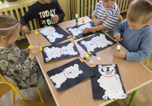 Czworo dzieci przy stole ozdabia swoje namalowane białe pieski