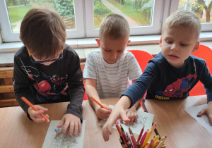 Trzech chłopców siedzi przy stole i rysuje
