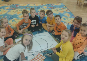 Dzieci siedzą wokół dużego rysunku dyni