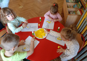 Dzieci przy stoliku wyklejają ilustracje warzy bibułą
