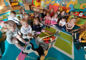 Dzieci siedzą w kole, a na środku dywanu znajduje się taca z warzywami