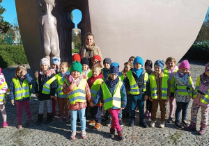 Grupa dzieci ubrana w kamizelki odblaskowe pozuje do zdjęcia na tle pomnika Pękniete Serce