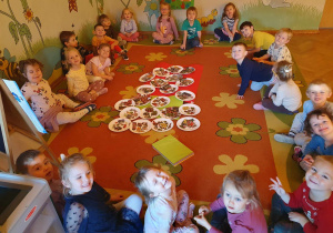Dzieci siedzą na dywanie w kole i prezentują swoje zdrowe i niezdrowe talerzyki i produktami