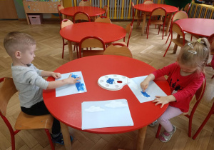 Chłopiec i dziewczynka wykonują przy stoliku pracę plastyczną ,,Deszczowe chmury" malując palcami