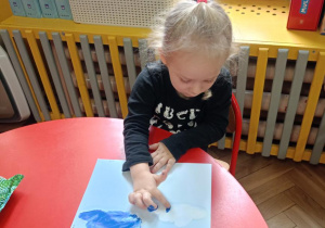 Dziewczynka wykonuje przy stoliku pracę plastyczną ,,Deszczowe chmury" malując palcami
