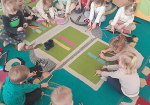 Dzieci układają na dywanie dowolne wzory/kształty z kredek