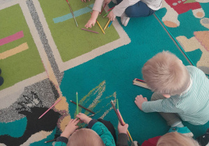 Dzieci układają na dywanie dowolne wzory/kształty z kredek