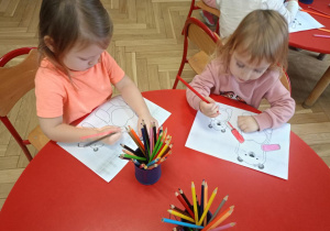 Dzieci przy stolikach kolorują ilustracje misi