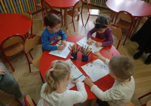 Dzieci przy stolikach kolorują ilustracje misi