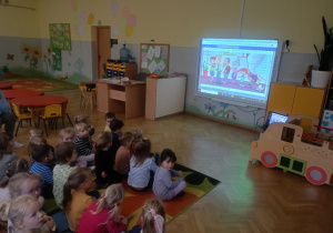 Dzieci oglądają na tablicy interaktywnej w gr 2 i bajki czytanej przez nauczyciela pt.,,Dlaczego mój brat jest wcześniakiem?"