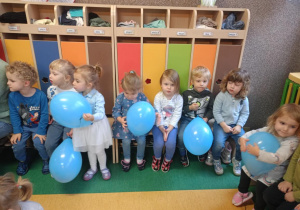 Dzieci siedzą na holu, trzymając niebieskie balony