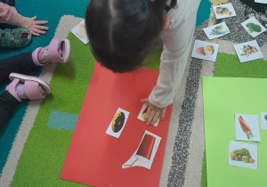 Dziewczynka przykleja na czerwony karton ilustrację niezdrowego produktu