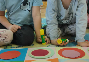 Dwóch chłopców przykleja na dużym kartonie kolorowe papierowe koła
