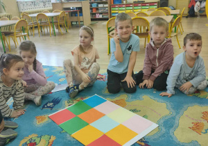 Dzieci siedzące na dywanie obok kolorowej szachownicy