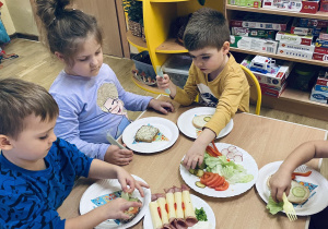 Dzieci siedzące przy stolikach przygotowują kanapki