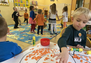 Chłopiec wyklejający pomarańczową bibuła narysowaną dynię