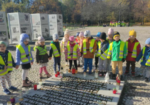 Dzieci w zielonych kamizelkach stoją nad pamiątkową tablicą w parku