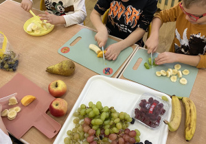 Dzieci kroją owoce siedząc przy stole