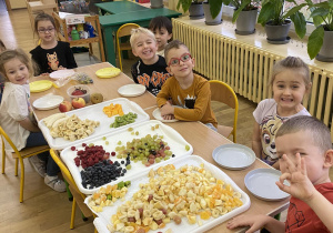 Dzieci siedzące przy stole obok trzech dużych tac z owocami