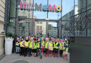 Grupa dzieci ubrana w kamizelki odblaskowe pozuje przez budynkiem Mediateki MEMO
