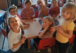 Grupa dzieci siedzi przy stolikach lepiąc z masy plastycznej
