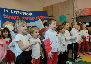 Grupa dzieci śpiewająca i trzymająca małe flagi Polski