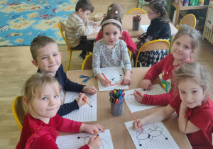 Pięcioro dzieci siedzi przy stole i koloruje obrazki z wizerunkiem Mikołaja