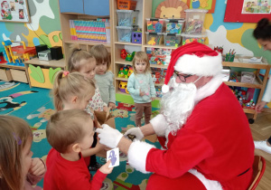 Mikołaj kolejno rozdaje dzieciom prezenty