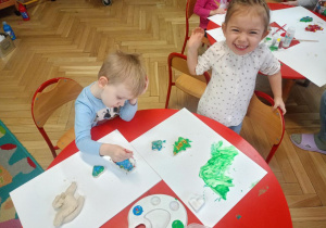 Dzieci przy stoliku malują i ozdabiają wyciśnięte foremkami świąteczne kształty