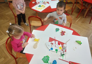 Dzieci przy stoliku malują i ozdabiają wyciśnięte foremkami świąteczne kształty