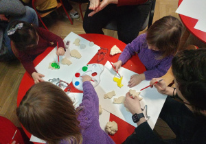 Dzieci z pomocą rodziców malują farbami wycięte przy pomocy foremek świąteczne wzory