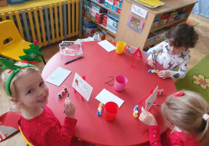 Mikołajki - dzieci siedzą przy stolikach i malują obrazki przedstawiające Mikołaja