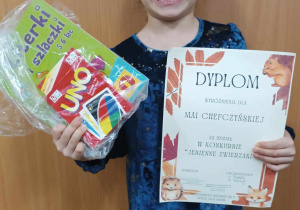 Dziewczynka prezentuje dyplom i nagrodę zdobyte w konkursie plastycznym