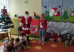 Pani i Mikołaj stoją obok siedzących na dywanie dzieci