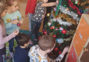 Dzieci dekorują choinkę bombkami