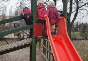 Zabawy w ogrodzie przedszkolnym - troje dzieci stoi na urządzeniu ogrodowym