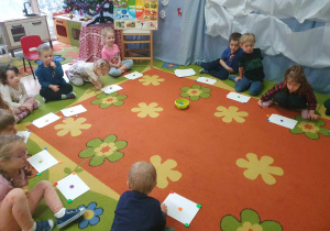 Zabawy z guzikami - dzieci siedzą na dywanie i układają tyle guzików na kartonie ile dźwięków usłyszą