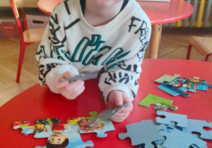 Chłopiec układa przy stole puzzle