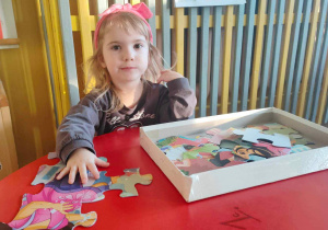 Dziewczynka układa przy stole puzzle