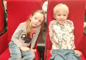 Dziewczynka i chłopiec siedzący na czerwonych fotelach teatralnych