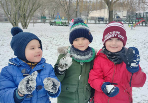 Trzech chłopców ubranych w zimowe ubrania stojący w ogrodzie przedszkolnym