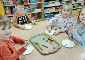 Czworo dzieci siedzi przy stole i lepi z plasteliny