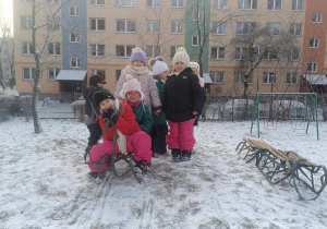 Grupa dzieci ubrana w zimowe stroje stoi na ośnieżonej górce