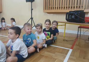 Dzieci siedzą na podłodze w sali gimnastycznej