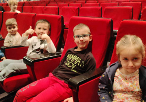 trzech chłopców i dziewczynka siedzą na czerwonych teatralnych krzesłach