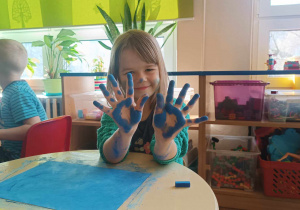 Dziewczynka pokazuje dłonie ubrodzone w czasie pracy suchymi pastelami