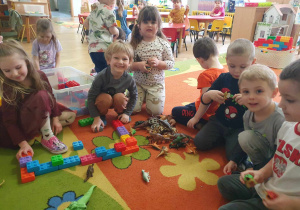Dzień Dinozaura - dzieci siedzą na dywanie i budują z klocków domy dla dinozaurów