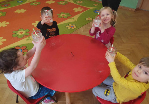 Hodowla kryształków - dzieci siedzą przy stolikach i pokazują swoje słoiczki z roztworem z soli