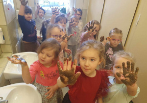 Eksperyment z olejem i piaskiem - dzieci są w toalecie i pokazują ręce umoczone w oleju i piasku